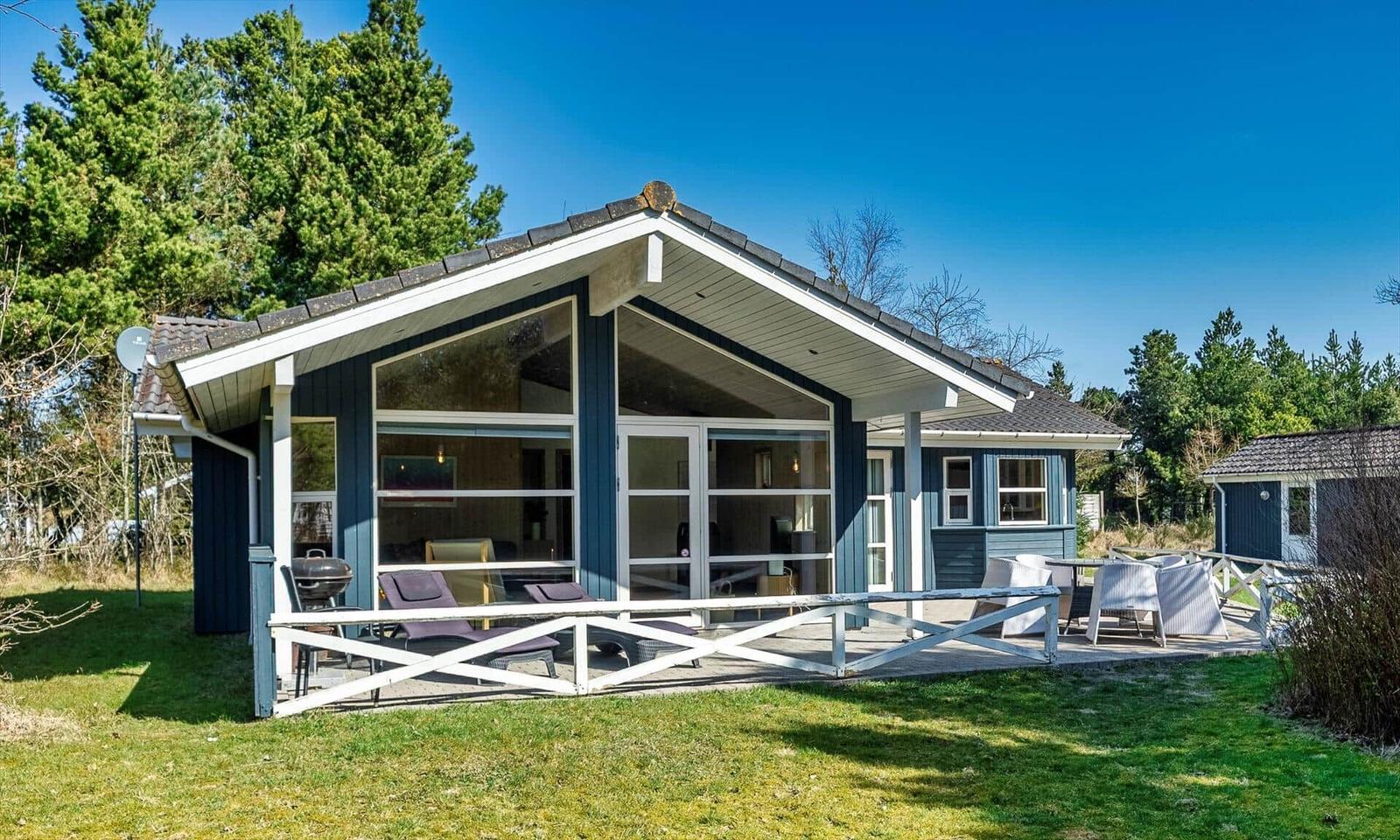 Ein blau-weißes Ferienhaus mit großem Glasbereich und Terrasse mit Gartenmöbeln.