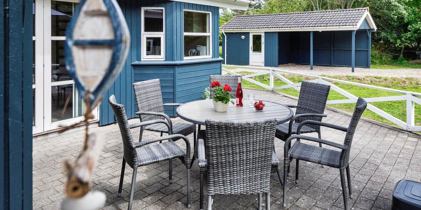 Terrasse mit Tisch und Stühlen vor blauem Haus. Hinterhof mit weißem Zaun und kleinem Schuppen.