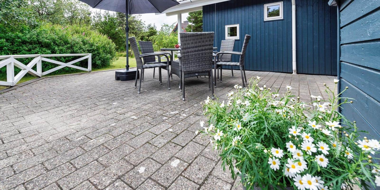 Terrasse mit Sitzgruppe, Sonnenschutz und Blumenbeet vor blauem Haus.