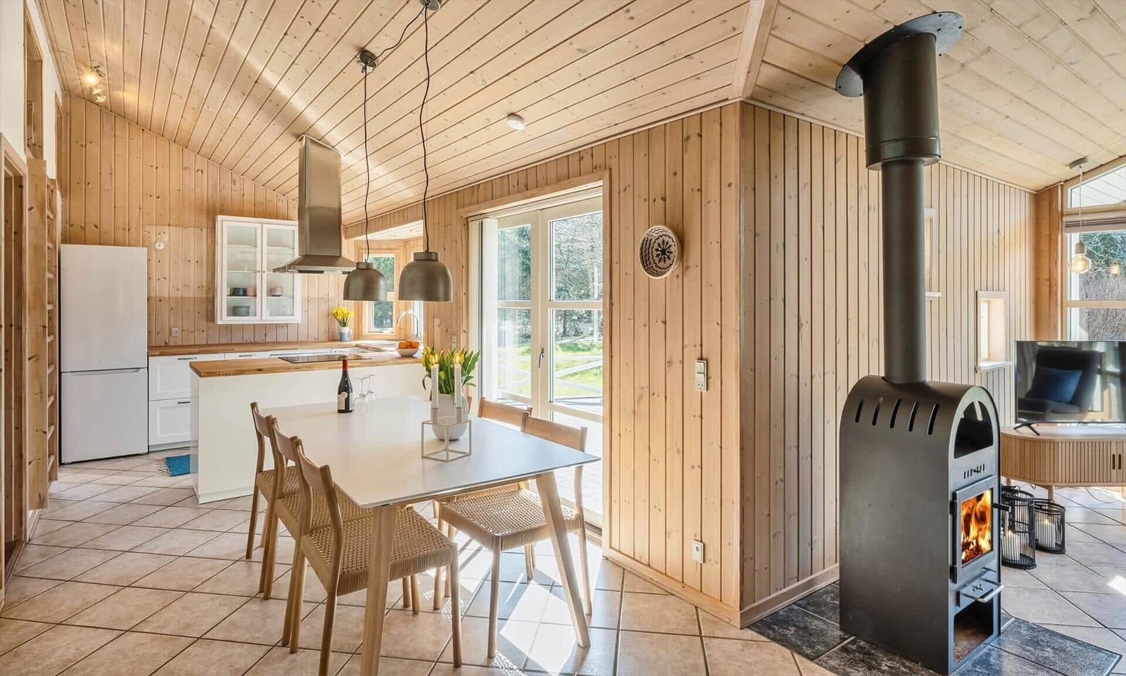 Küche mit Essbereich und Holzofen. Holzwände, Fenster und Tisch.