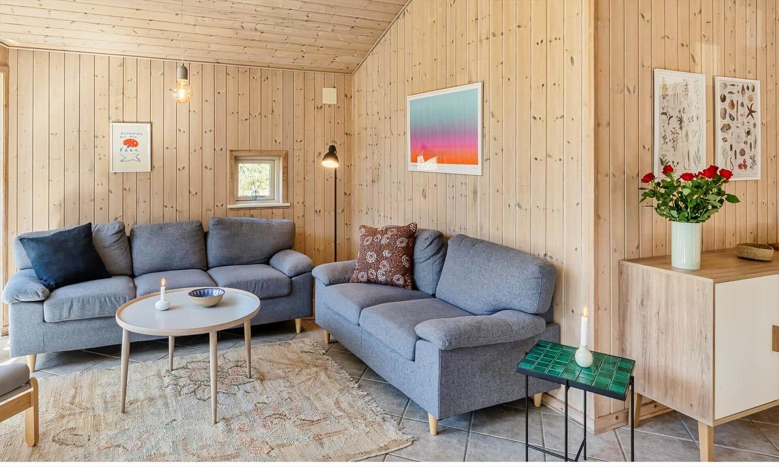 Wohnzimmer mit zwei grauen Sofas, Holzwänden und einem runden Tisch.