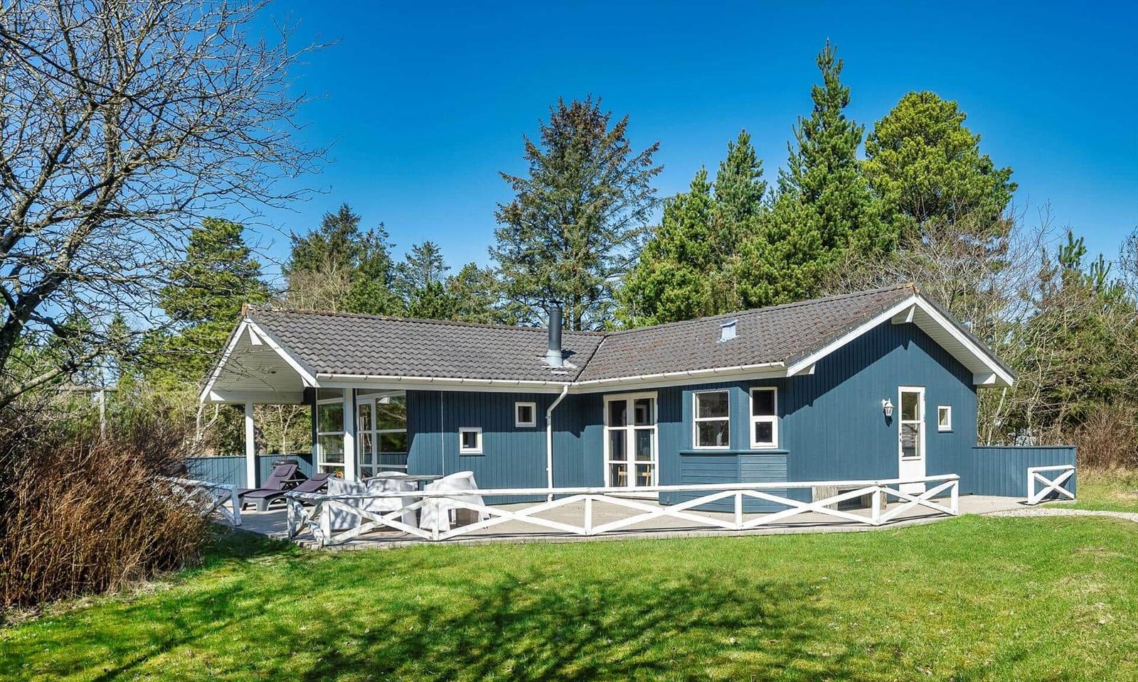 Blauer Ferienhaus mit Terrasse und Garten. Umgeben von Bäumen und Gras.