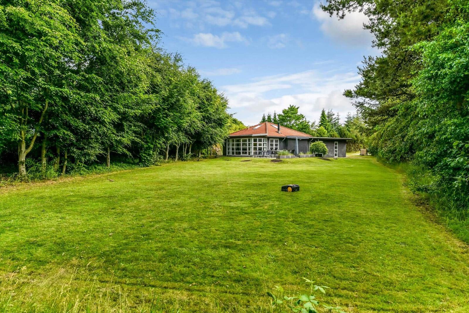 Haus mit rotem Dach und großem Garten zwischen Bäumen.