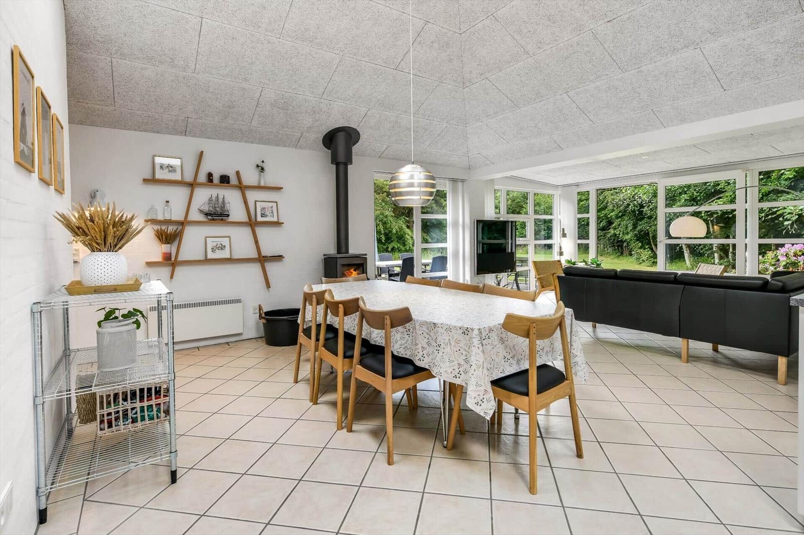 Großer Raum mit Esstisch, Sofa und Kamin. Fenster bieten Blick auf Garten.