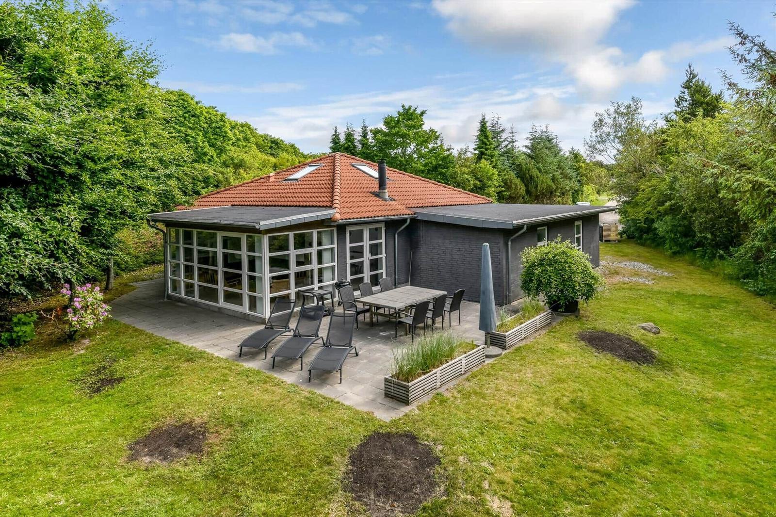 Moderne Villa mit Terrasse, Garten und Grillplatz. Umgeben von Bäumen und Grasflächen.
