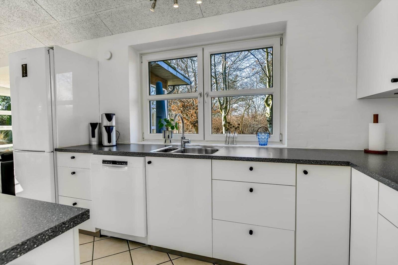 Küche mit weißer Einbauküche, dunkler Arbeitsplatte und Fensterblick auf Bäume.