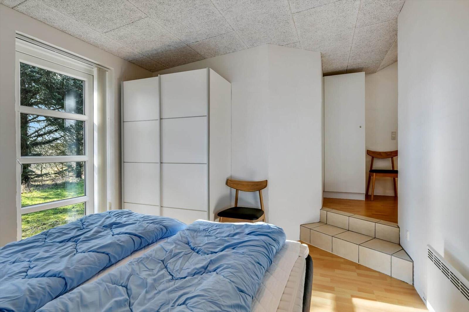 Schlafzimmer mit Bett, Kleiderschrank und Fenster zum Garten.
