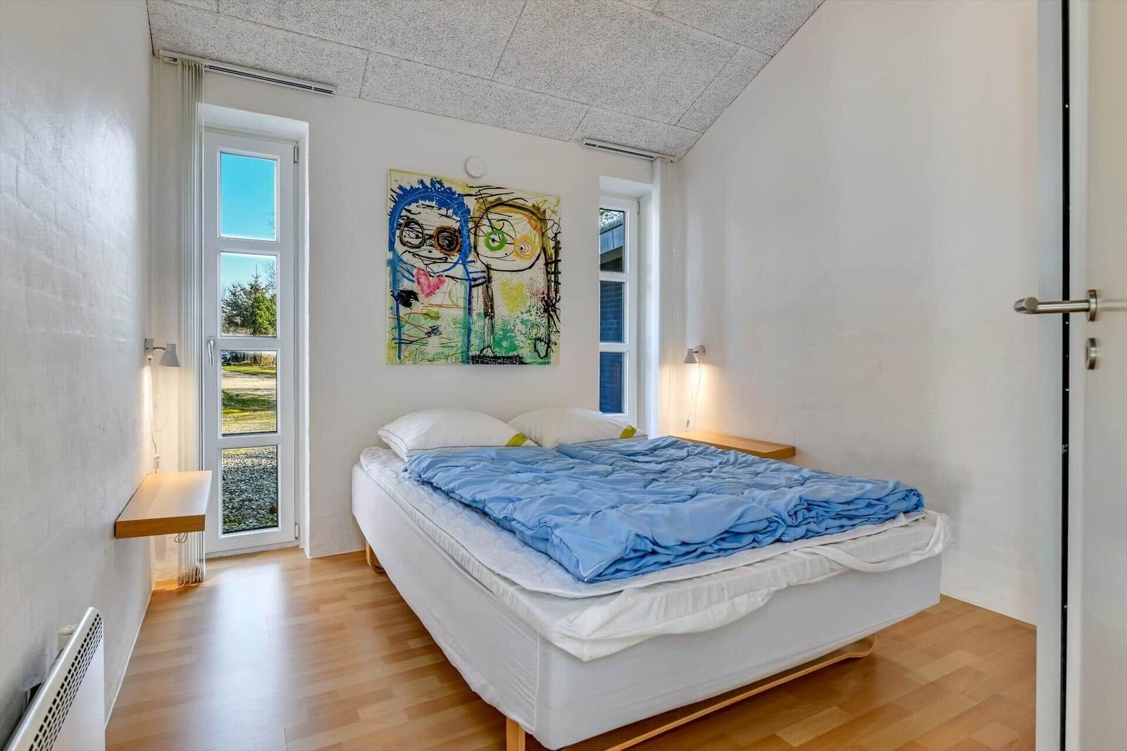 Schlafzimmer mit Bett, Wandbild und Fenstern.