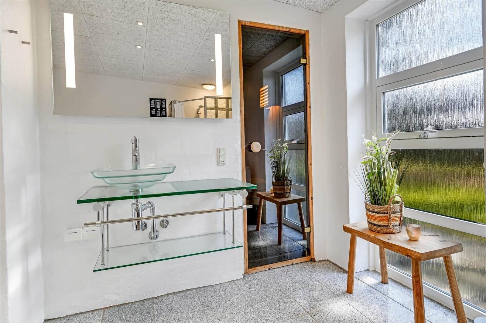 Badezimmer mit Glaswaschbecken, Spiegel und Pflanze vor Fenster