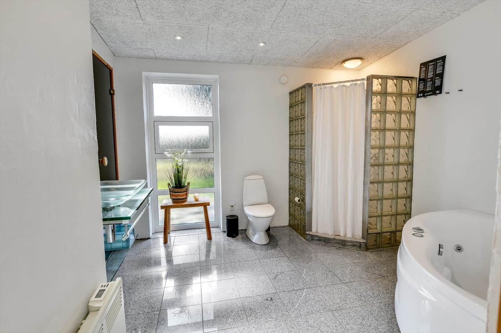 Badezimmer mit Badewanne, Dusche und Toilette. Fenster, Pflanze und Waschtisch sichtbar.