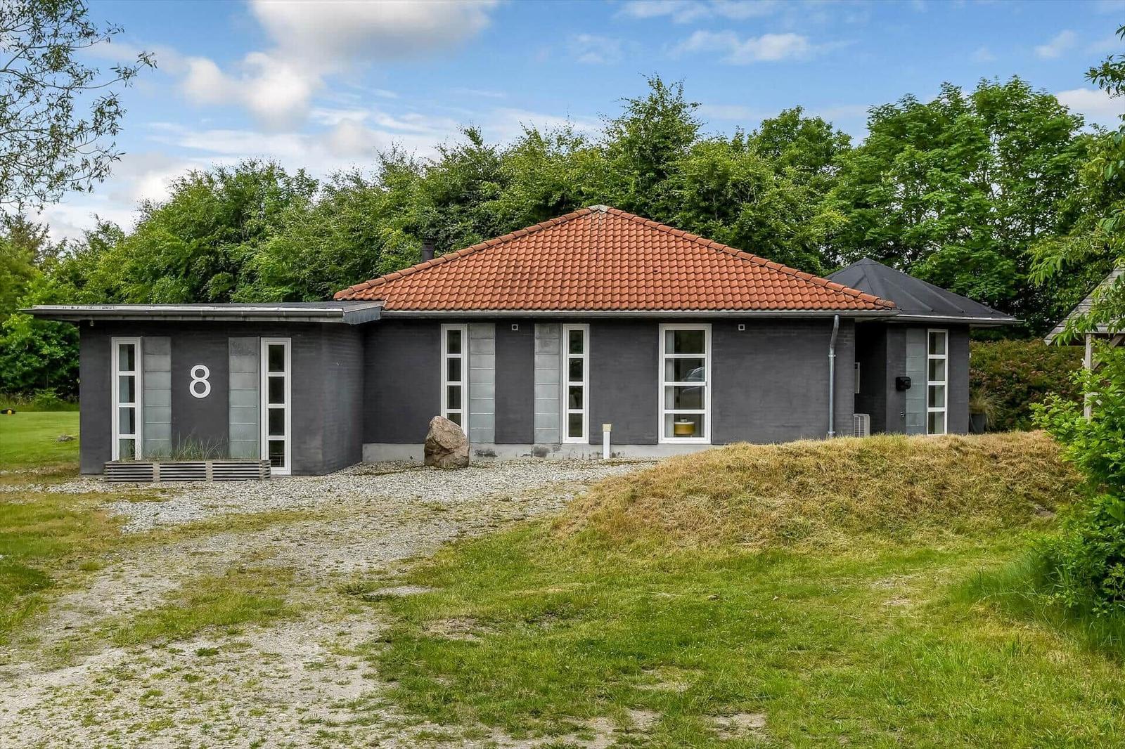Moderne Villa mit rotem Dach und grauer Fassade. Grün umgeben mit Rasen und Bäumen.