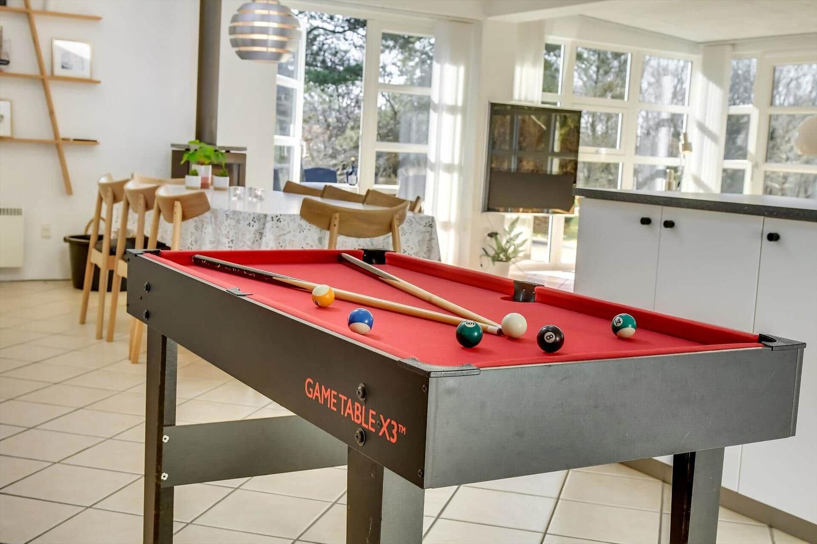Pooltisch mit Kugeln und Stöcken im Wohnbereich mit Fenstern und Küchenzeile.