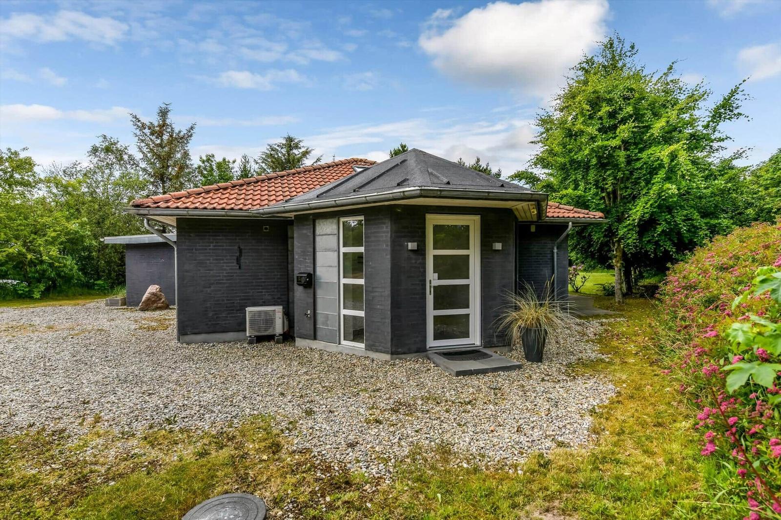 Moderne Villa mit dunklem Stein und rotem Dach, umgeben von Grün und Blumen.