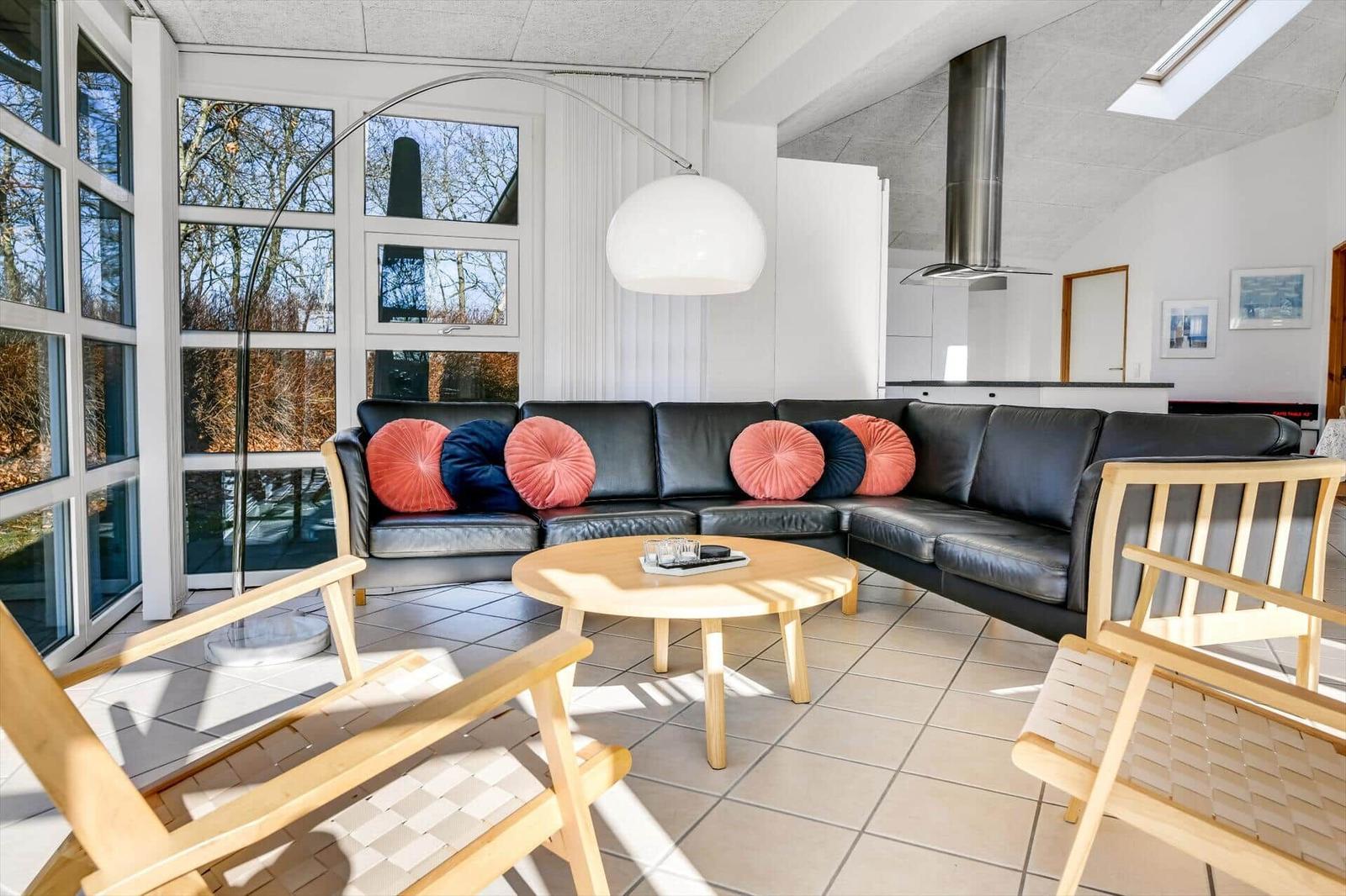 Wohnzimmer mit schwarzer Couch, Holzstühlen und großem Fenster