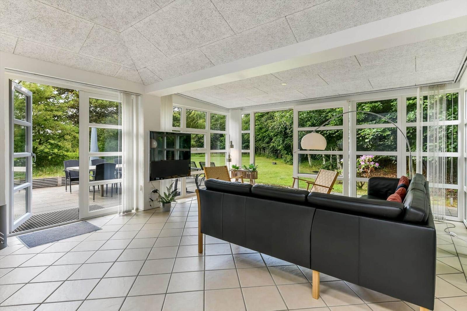 Wohnzimmer mit schwarzer Ledercouch, großen Fenstern und Blick auf Garten