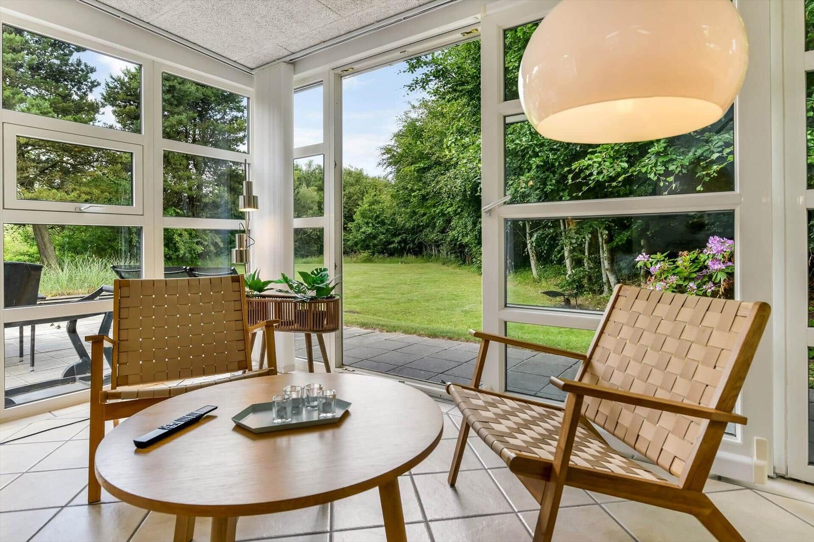 Sitzbereich mit zwei Stühlen und Tisch. Große Fenster mit Blick auf Garten.