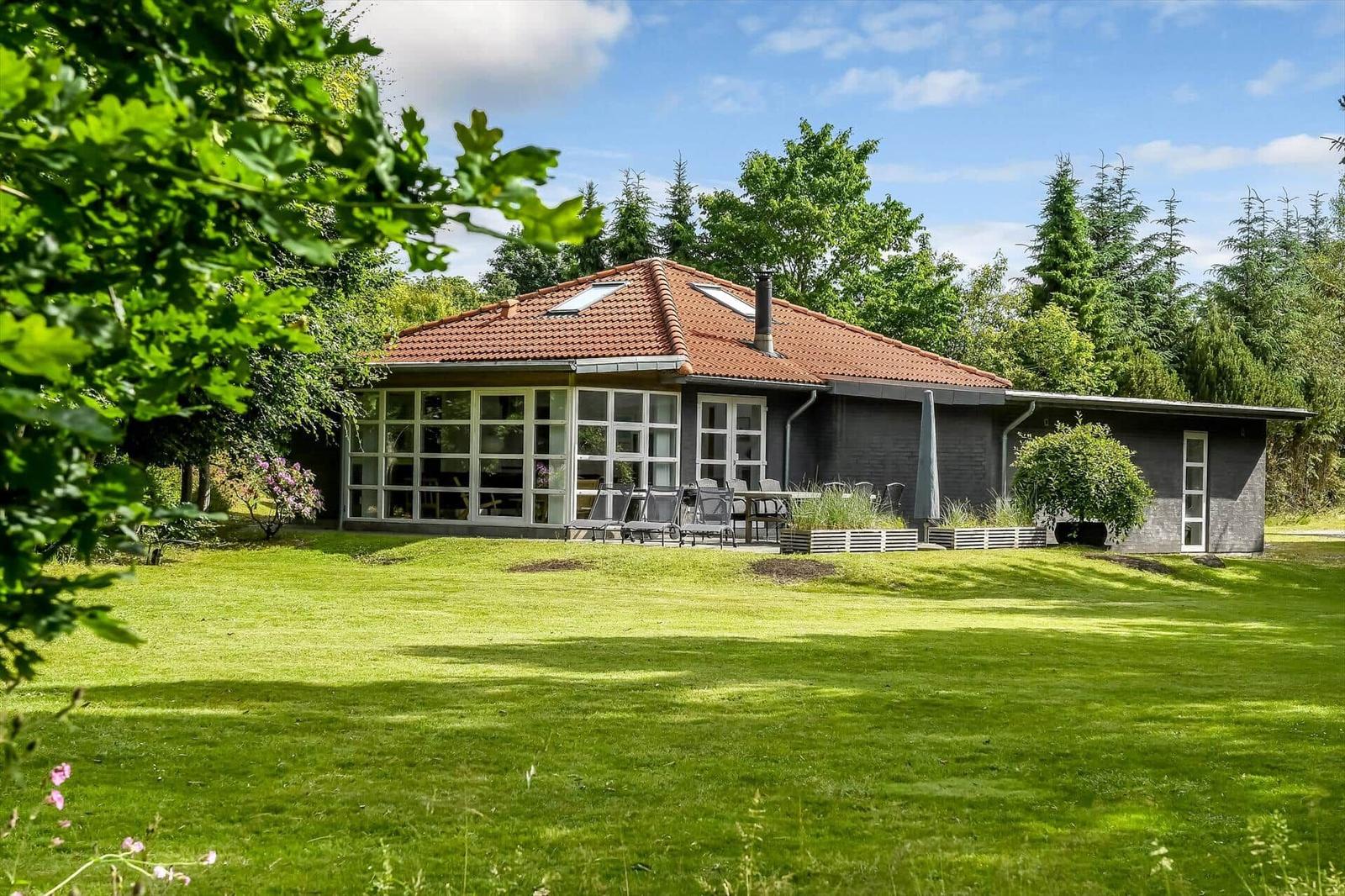 Haus mit rotem Dach, großem Glasbereich und Garten mit Liegestühlen.
