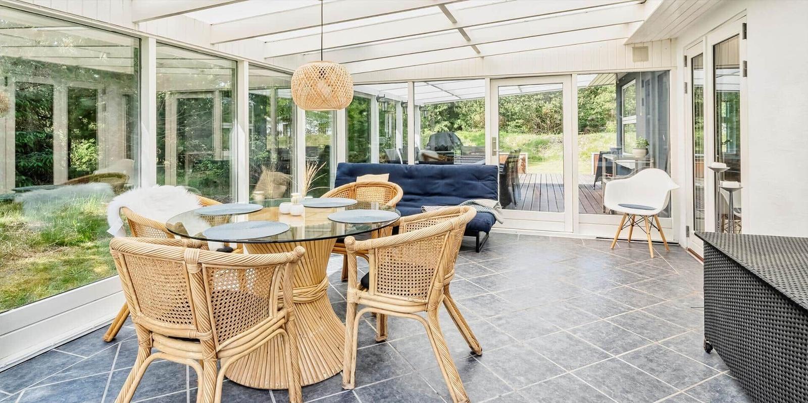 Terrasse mit Esstisch, Stühlen und Sofa. Glaswände und Decke. 