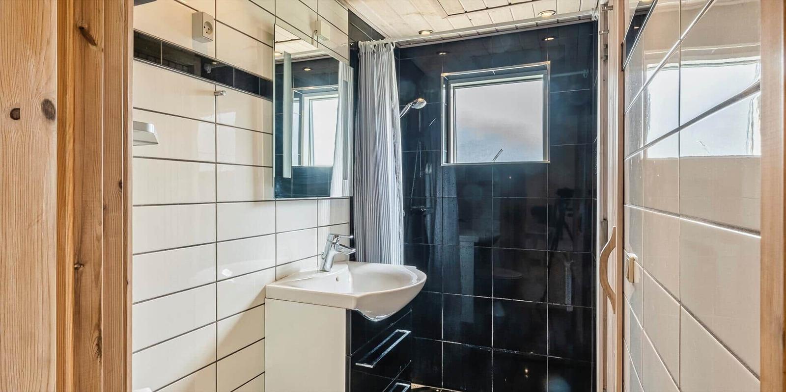 Badezimmer mit Dusche, Waschbecken und Spiegel. Schwarze Fliesen und Holzelemente.