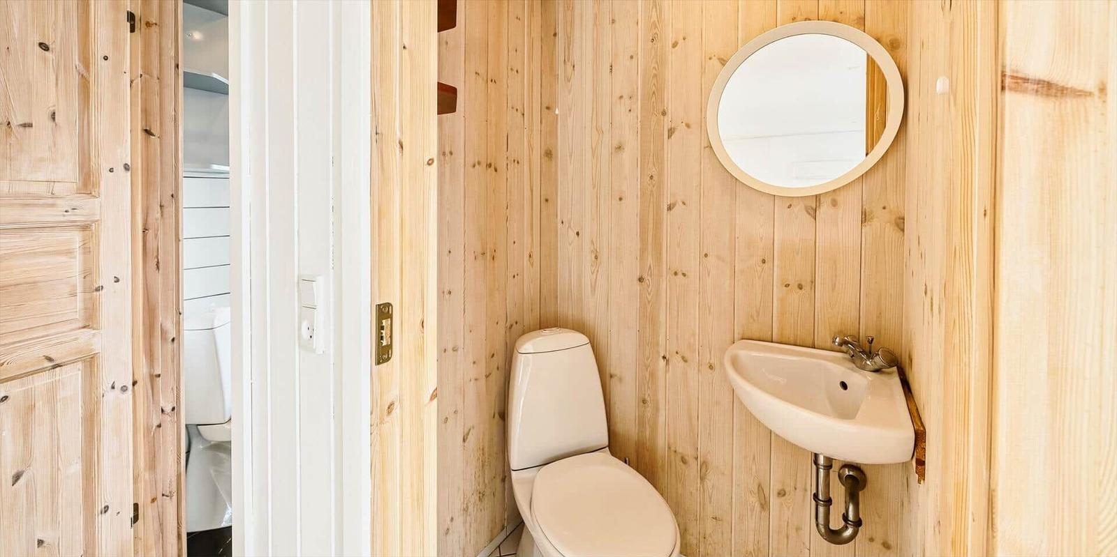 Badezimmer mit Toilette, Waschbecken und runden Spiegel an Holzwand