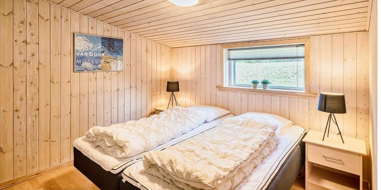 Schlafzimmer mit Holzwand, Bett und Fenster mit Blick auf Grün.