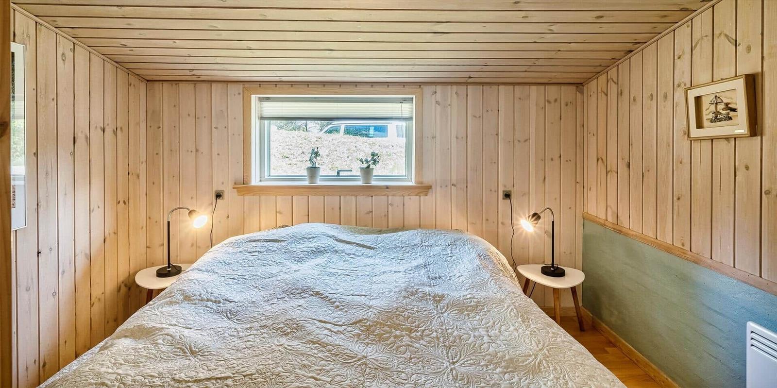 Schlafzimmer mit Holzwandverkleidung, Bett und Fenster mit Pflanzen.