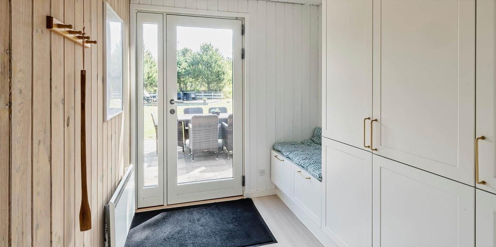 Eingangsbereich mit Glastür, Holzwand und weißen Schränken mit Sitzbank.