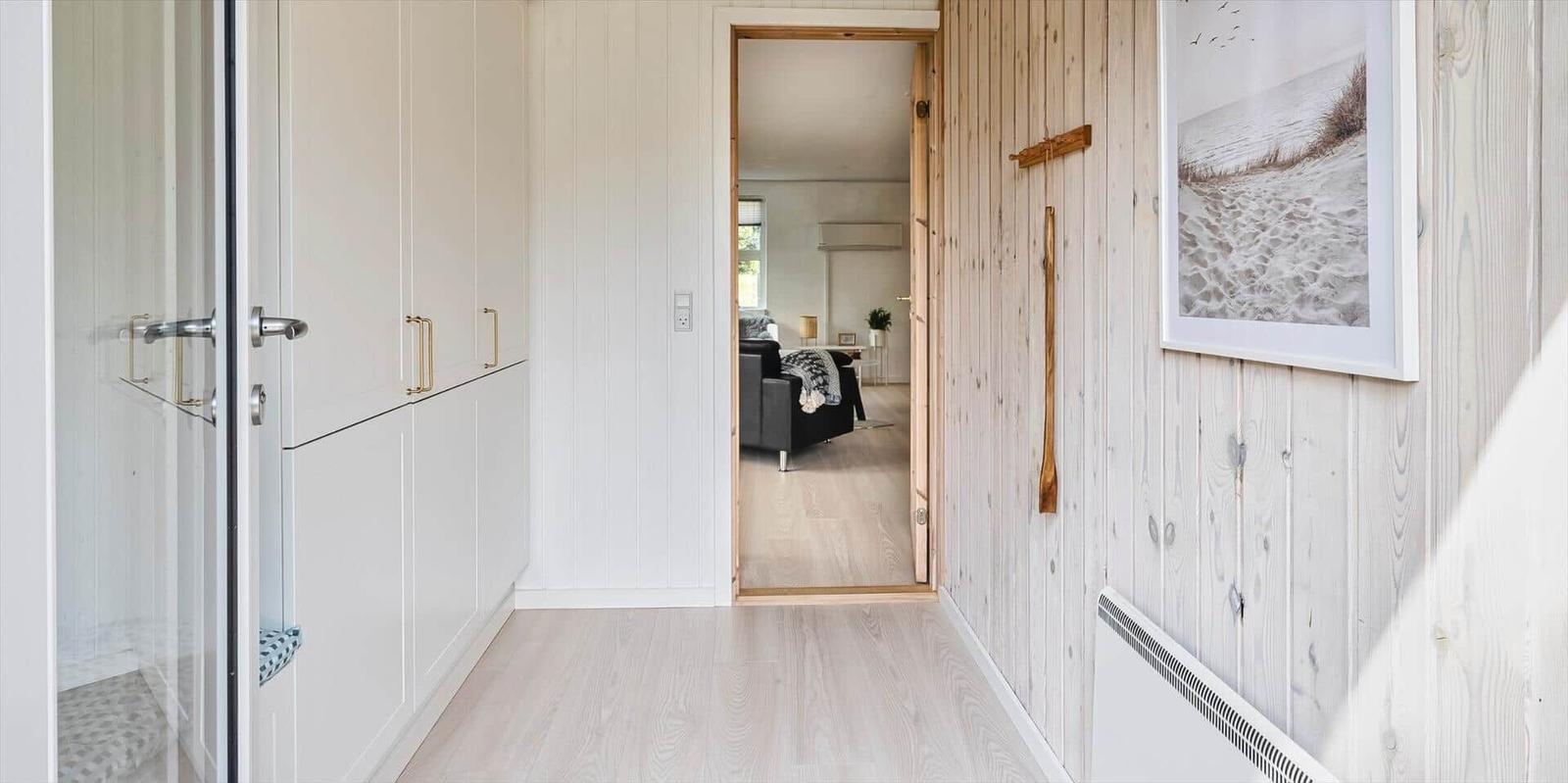 Flur mit Holzwand, Spiegel und Blick in Wohnzimmer mit Sofa.