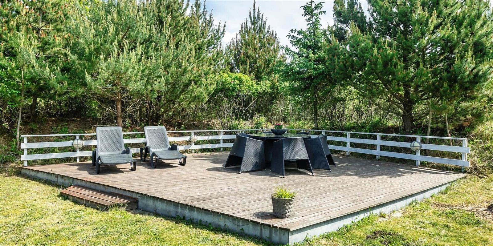 Holzterrasse mit Liegestühlen und Tisch, umgeben von Nadelbäumen.