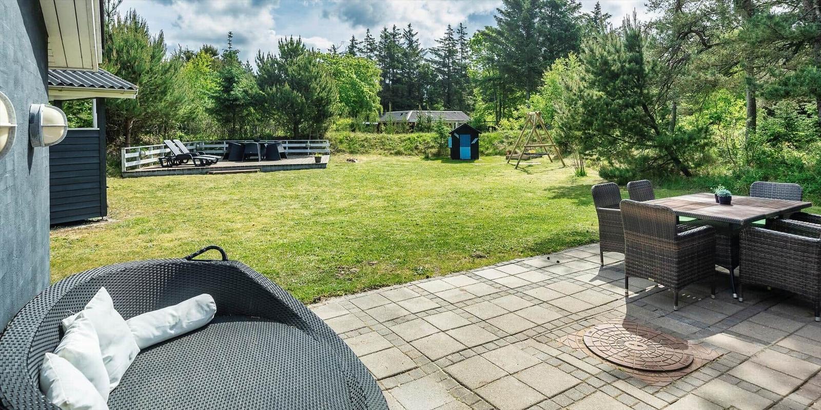 Terrasse mit Sitzgruppe und Blick auf grünen Garten mit Schaukel und Spielhaus.