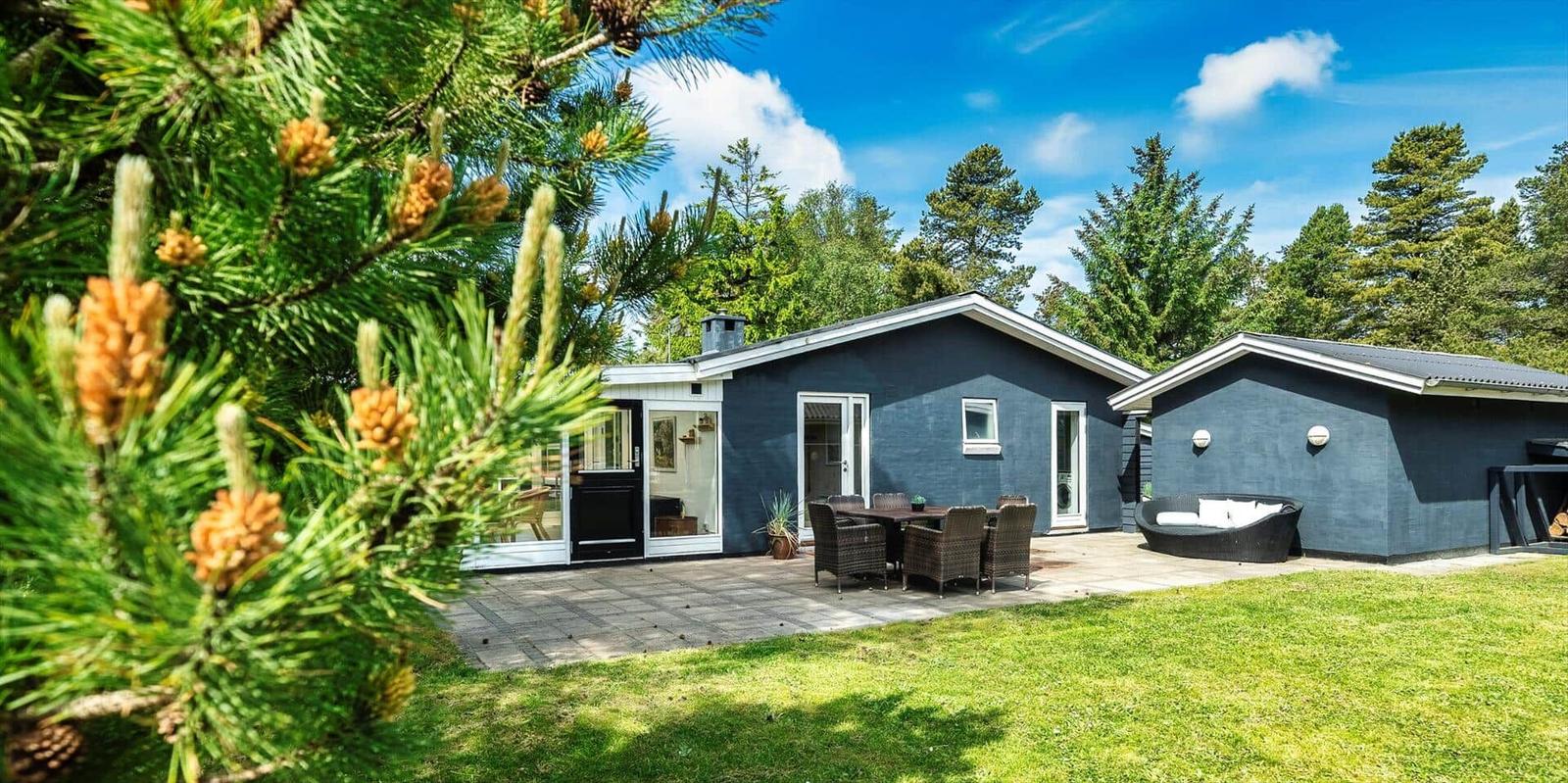 Ein Haus mit Terrasse, Garten und Sitzgelegenheiten unter Bäumen.