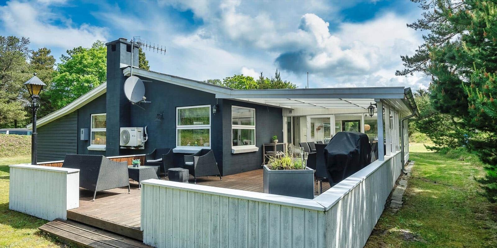 Ein Haus mit Terrasse, Sitzgelegenheiten und Grillplatz im Freien.
