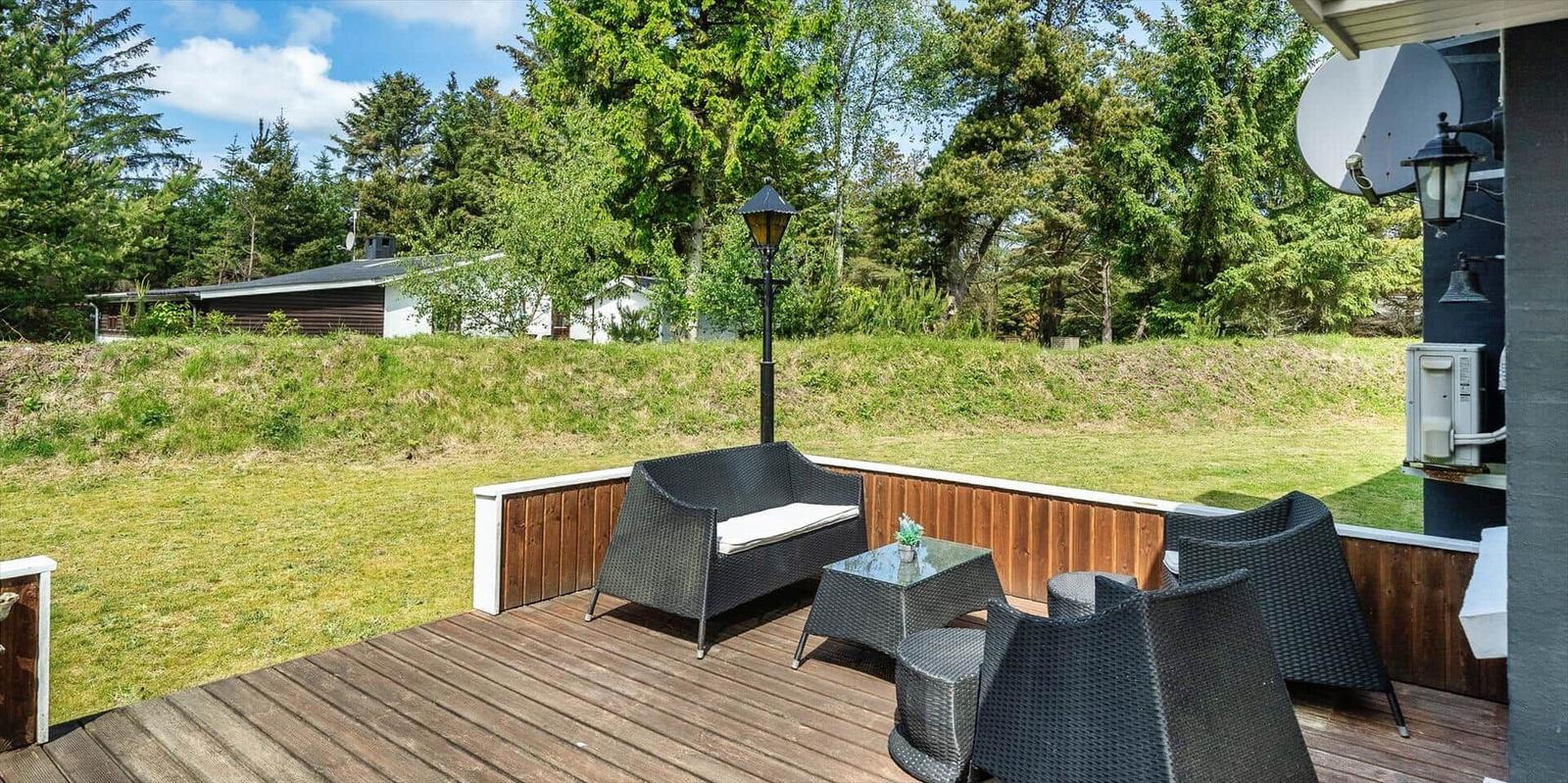 Terrasse mit Sitzgruppe, Tisch und Lampen. Hintergrund: Grasfläche und Bäume.
