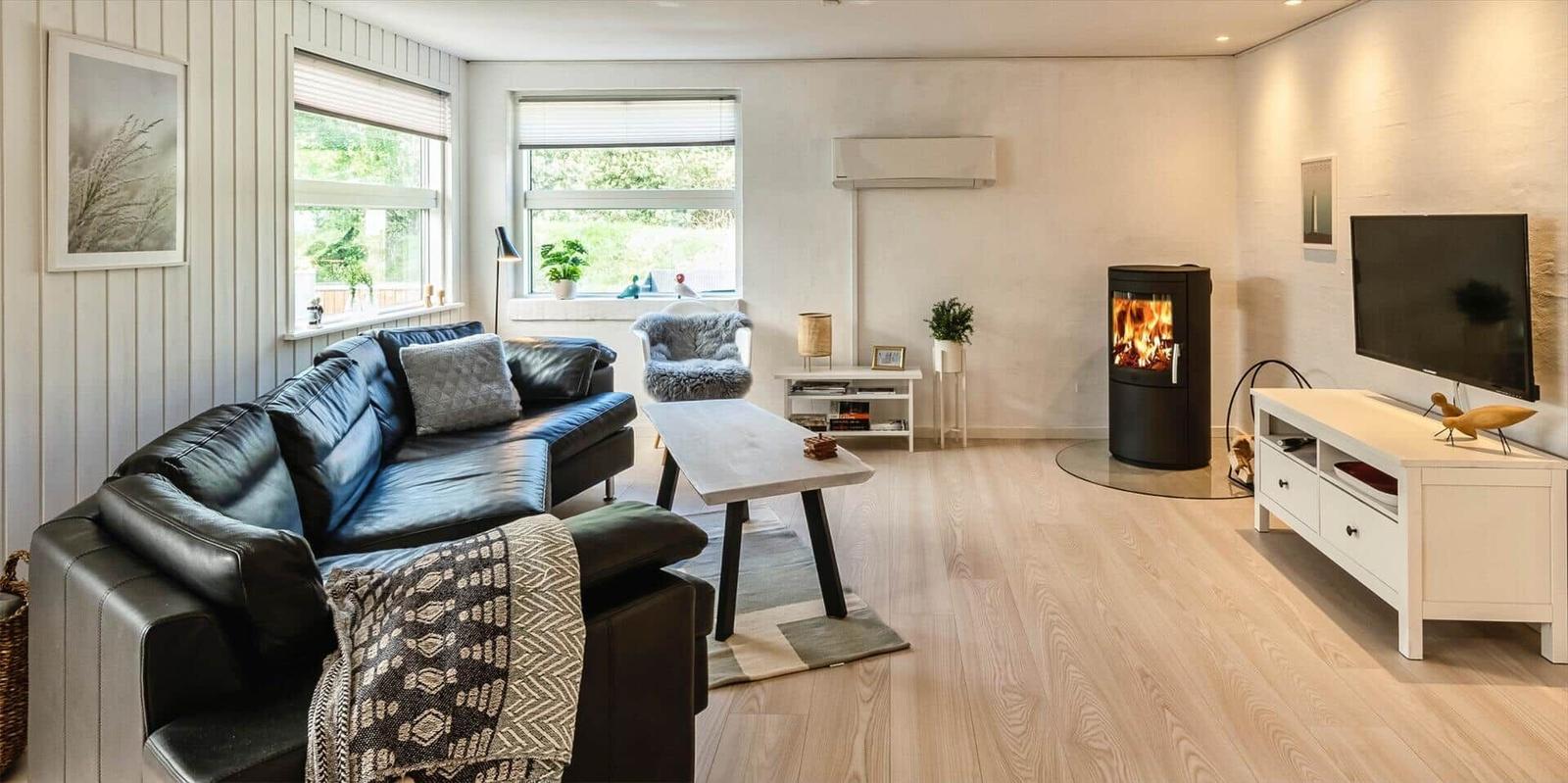 Wohnzimmer mit Sofa, Kamin und TV. Holzboden und große Fenster.
