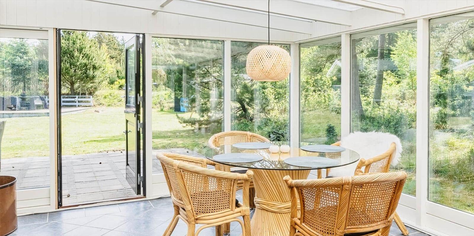 Terrassensitzgruppe mit Glasrundtisch und Rattanstühlen. Durchgehende Glaswände blicken auf Garten und Pool.