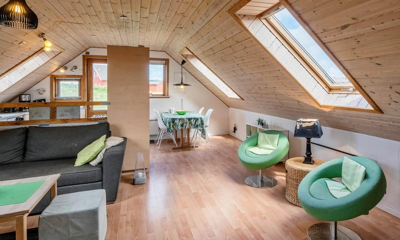 Dachgeschosswohnung mit Holzdecke, grünen Sesseln und Essbereich.