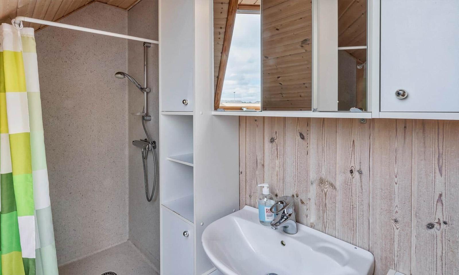 Bad mit Dusche, Waschbecken und Spiegelschrank. Holzwand und Duschvorhang mit Streifen.