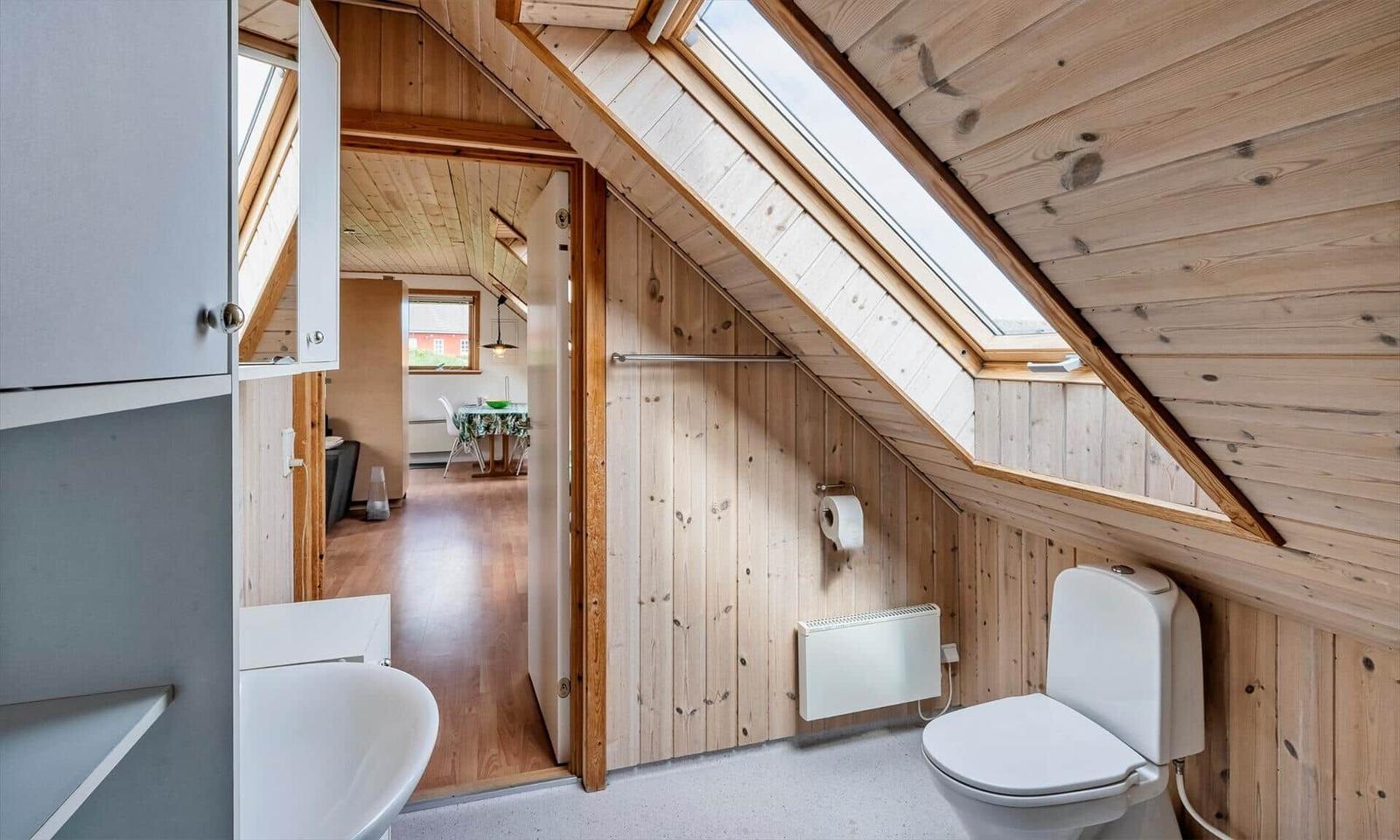 Badezimmer mit Toilette und Waschbecken unter Dachschräge mit Holzwandverkleidung und Dachfenster.