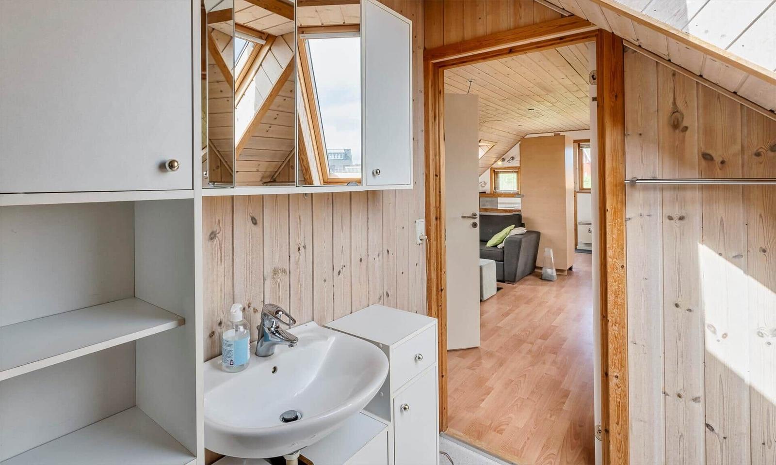 Badezimmer mit Waschbecken und Spiegelschrank. Durchgang in Wohnbereich mit Holzdecke.