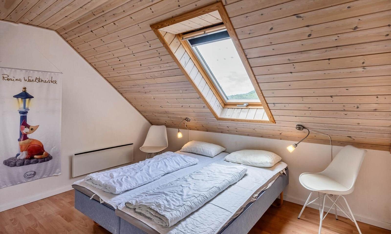 Schlafzimmer mit Dachschrägen, Dachfenster und zwei weißen Stühlen.