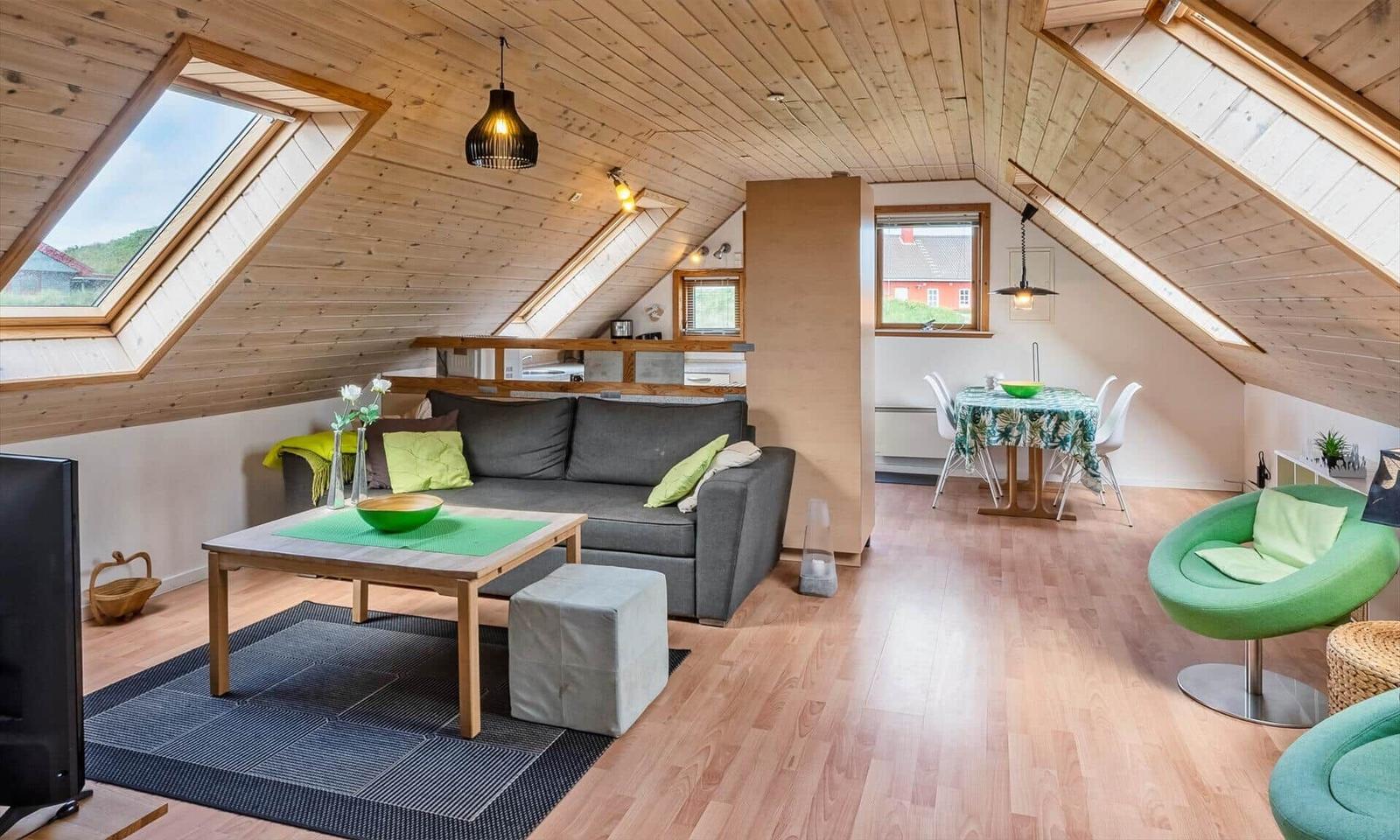 Dachgeschosswohnung mit Sofa, Esstisch und grünen Sesseln. Holzdecke und große Dachfenster.