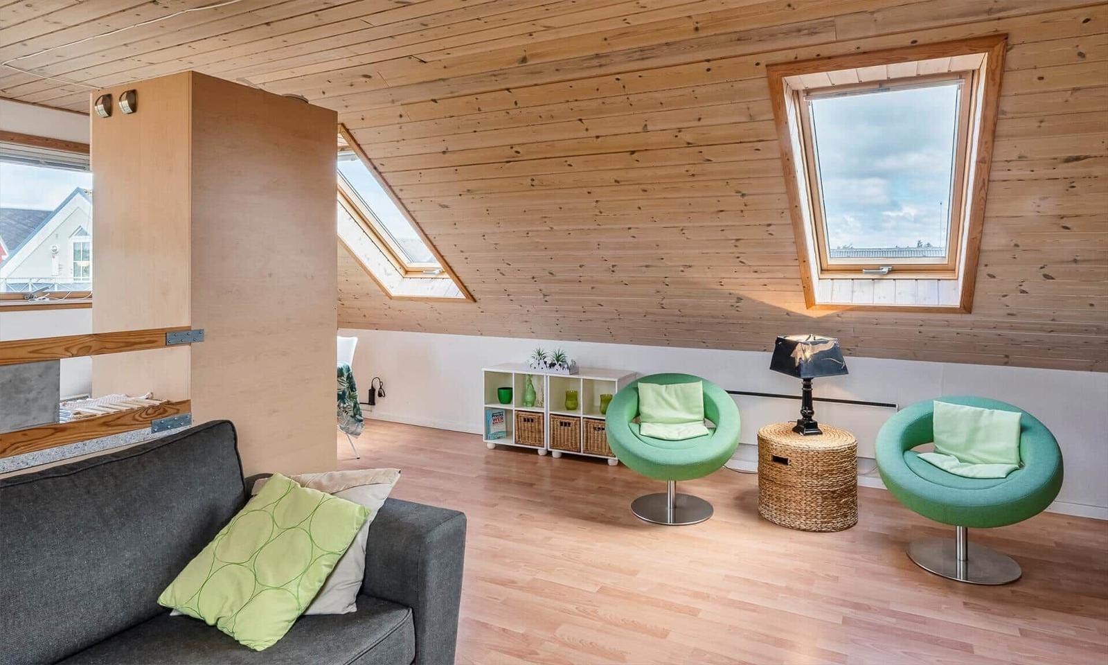 Wohnraum mit Holzdecke, grünen Sesseln und Dachfenstern.