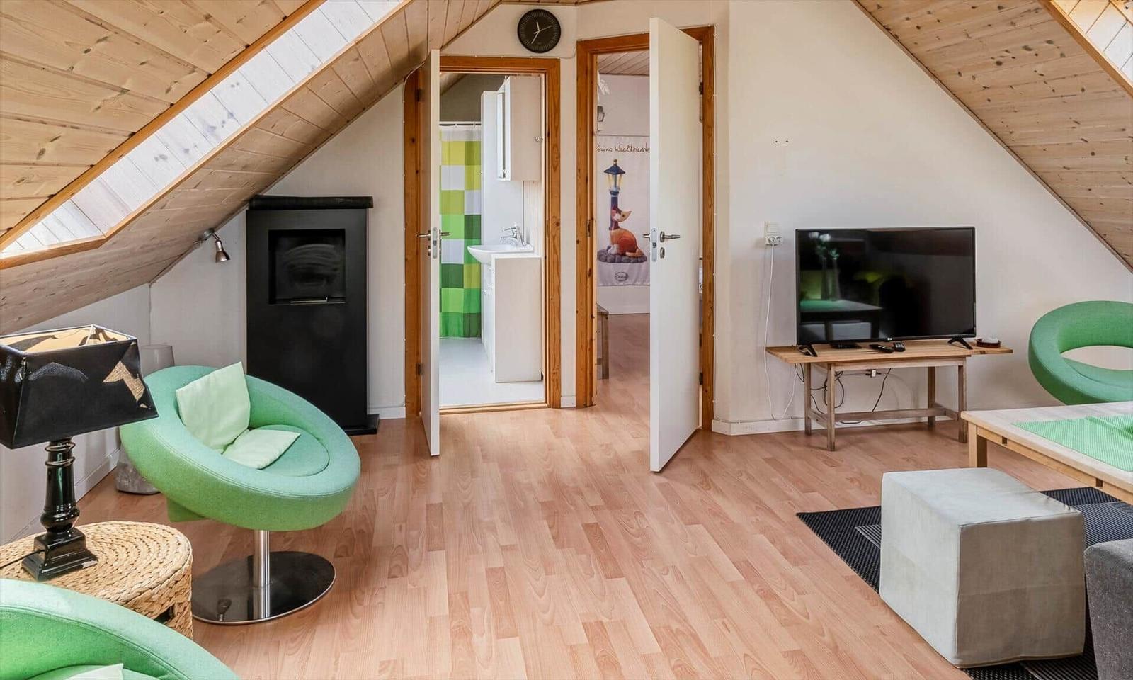 Wohnbereich mit TV, grünen Sesseln und Holzboden. Tür führt in Bad und Schlafzimmer.