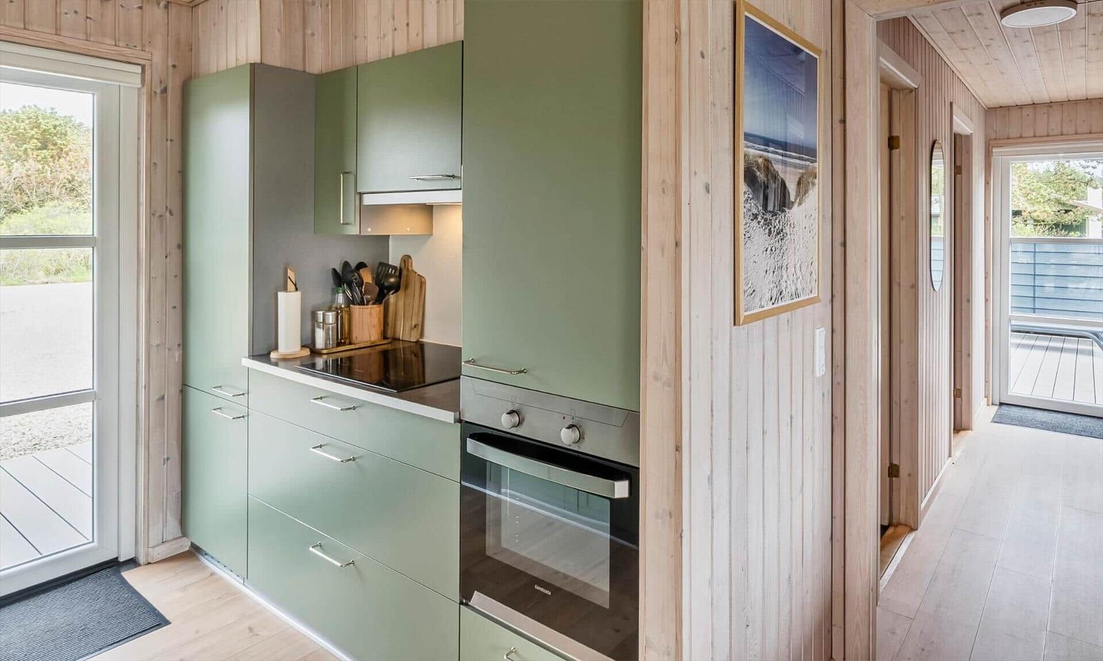 Küche mit grünen Schränken, Herd und Backofen. Holzwände und Tür zum Balkon.