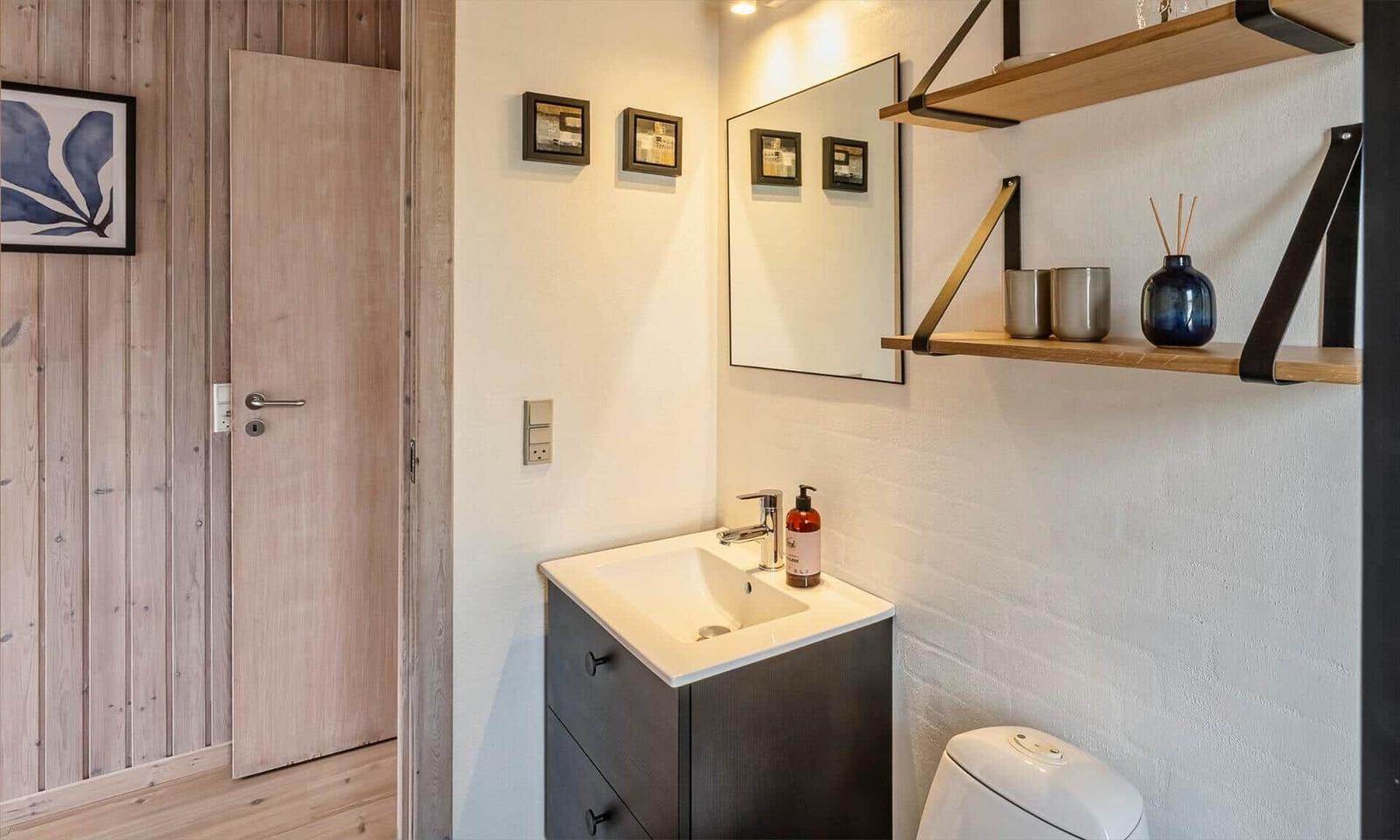 Badezimmer mit Waschbecken, Spiegel und Holzregalen an der Wand.