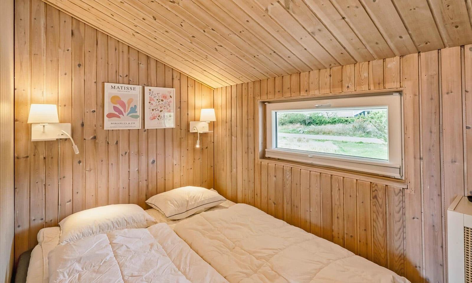 Schlafzimmer mit Holzwand und Fenster. Bett mit Kissen und Decke.