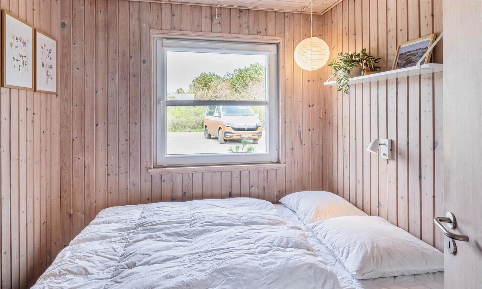 Schlafzimmer mit Holzwand, Fenster und Bett. Draußen steht ein gelber Van.