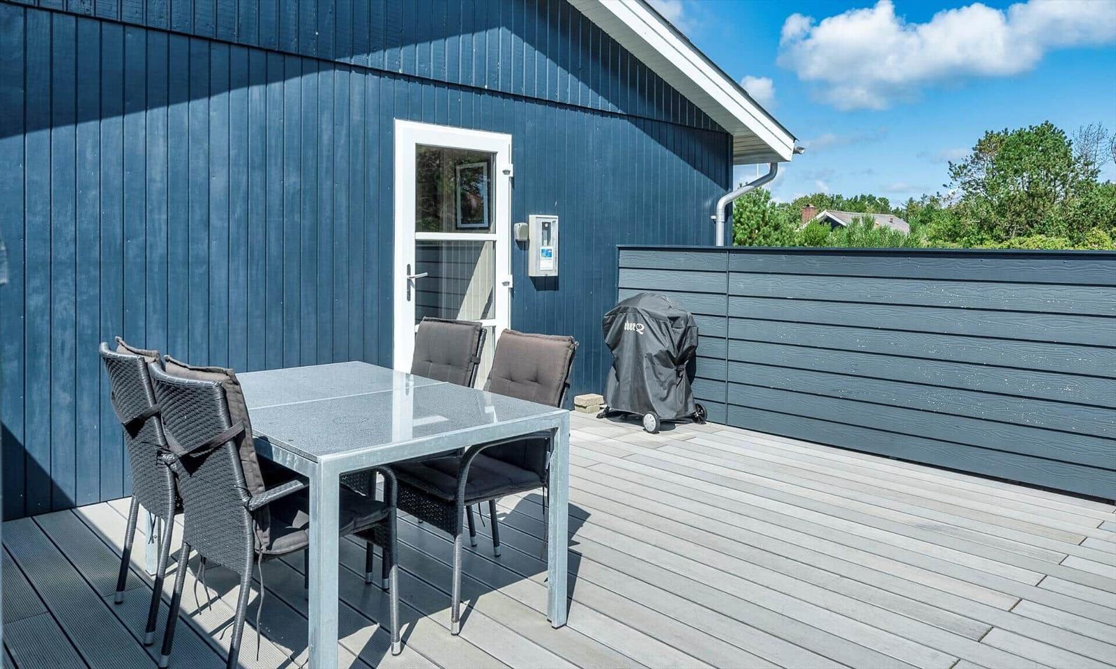 Terrasse mit Tisch, Stühlen und Grill. Blauer Holzaufbau und Holzdecke.