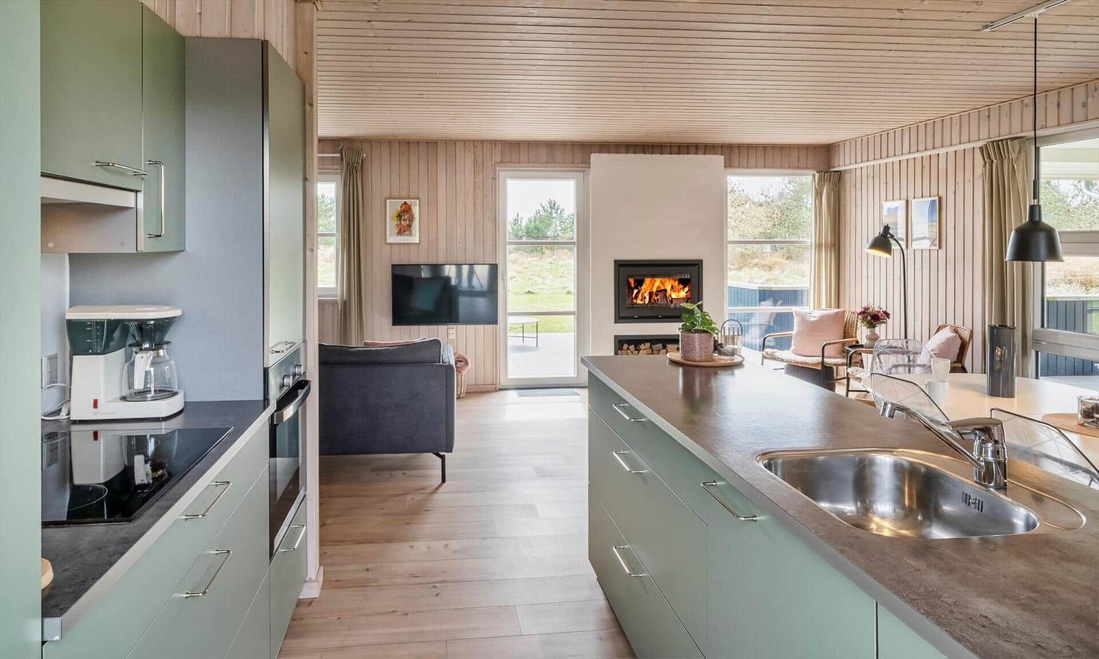 Küche mit Arbeitsplatte und Spüle. Im Hintergrund Wohnbereich mit Kamin und Fernseher.