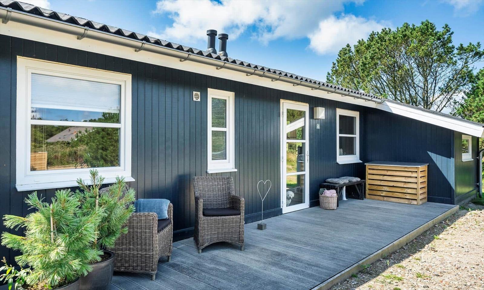 Ein dunkelblauer Holzhaus mit Terrasse, zwei Stühlen und Pflanzen.